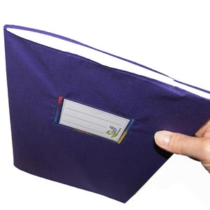 May include: A deep purple fabric-covered notebook featuring a rectangular white label with four horizontal lines for writing. The label is stitched onto the cover with multi-colored thread and includes the green text "Stoff" and "notizbuch".