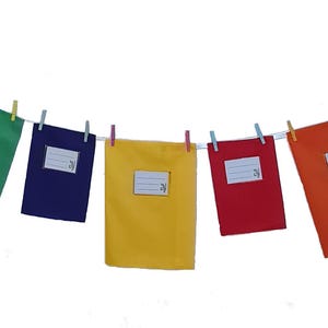 May include: A series of seven rectangular fabric pouches in blue, green, purple, yellow, red, orange, and black, each featuring a white rectangular label with horizontal lines for writing, all suspended from a white string by small colorful clothespins.