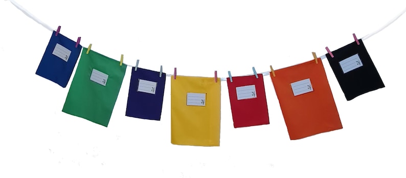 May include: A series of seven rectangular fabric pouches in blue, green, purple, yellow, red, orange, and black, each featuring a white rectangular label with horizontal lines for writing, all suspended from a white string by small colorful clothespins.