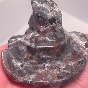 May include: A carved stone witch hat sculpture. The hat is primarily dark gray with reddish-brown and white veining throughout. The hat has a wide brim and a tall, pointed crown, and is a unique decorative item.