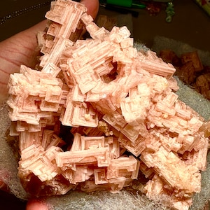 Puede incluir: Un cúmulo de cristales de sal rosa del Himalaya con una estructura geométrica apilada. Los cristales son translúcidos y tienen un aspecto delicado y en capas.