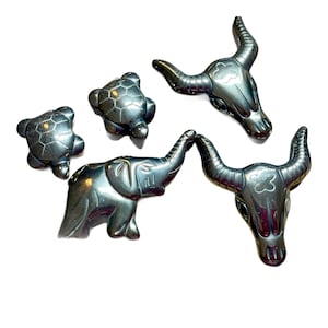 May include: Five small, black, polished stone animal figurines. The figurines are of a turtle, an elephant, and two bull skulls. Each figurine has a flower carved into its surface.