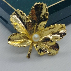 May include: A gold-tone leaf brooch with a single white pearl in the center.