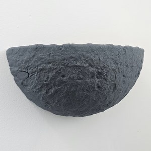 May include: A dark grey, textured, half-sphere wall sconce with a small hole on the side.