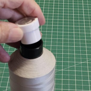 Pu&ograve; includere: Una grande bobina di filo grigio chiaro con un nucleo in plastica nera e un tappo in plastica bianca rimovibile. Il filo &egrave; avvolto strettamente attorno alla bobina cilindrica, posizionata in verticale per mostrare la trama del materiale.