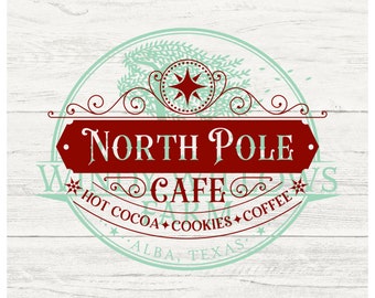 May include: A red and green vintage-style logo for a cafe called "North Pole Cafe". The logo features a stylized evergreen tree with a star and the text "North Pole Cafe" in a red banner. The text "Hot Cocoa, Cookies, Coffee" is below the banner. The text "Alba, Texas" is at the bottom of the logo.