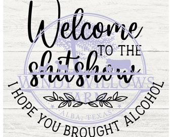 May include: A wooden sign with a white background and a distressed wood grain pattern. The sign features a circular design in lavender with the words "Welcome to the Shitshow" and "I Hope You Brought Alcohol". The sign also includes the words "Windy Willows Farm" and "Alba, Texas".