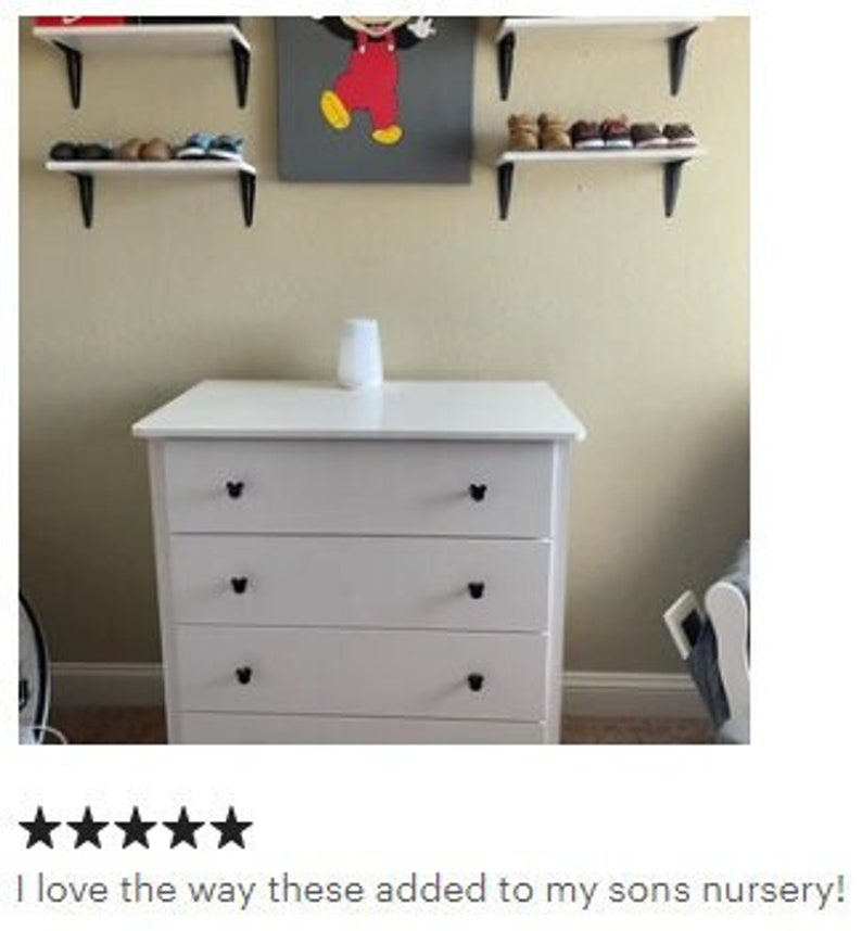 Op de afbeelding: Een witte ladekast met drie laden en zwarte hartvormige knoppen. Boven de kast bevinden zich drie planken met schoenen. Een ingelijste afbeelding van Mickey Mouse hangt aan de muur. Een witte luchtbevochtiger staat erop.