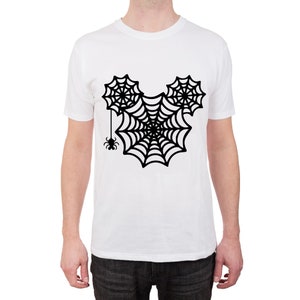 May include: White t-shirt with a black spiderweb design in the shape of Mickey Mouse ears. A small black spider hangs from the bottom of the web.