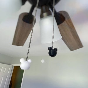 Może przedstawiać: Dwa łańcuszki do wentylatora sufitowego z uchwytami w kształcie głowy Myszki Miki. Jeden uchwyt jest czarny, a drugi biały.