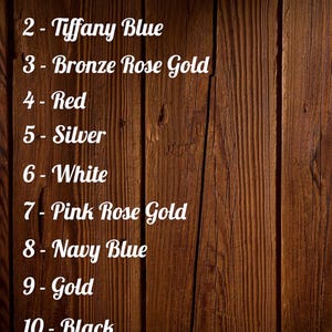 Op de afbeelding: Een houten achtergrond met een lijst van tien kleuropties in witte tekst: Hout, Tiffany Blue, Bronze Rose Gold, Rood, Zilver, Wit, Pink Rose Gold, Marineblauw, Goud en Zwart. Het PhotoRoom-logo staat rechtsonder.