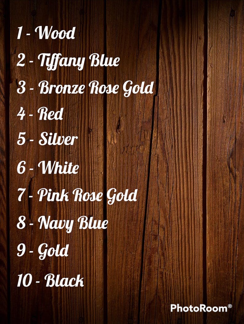 Op de afbeelding: Een houten achtergrond met een lijst van tien kleuropties in witte tekst: Hout, Tiffany Blue, Bronze Rose Gold, Rood, Zilver, Wit, Pink Rose Gold, Marineblauw, Goud en Zwart. Het PhotoRoom-logo staat rechtsonder.