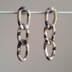 May include: A pair of long, dangling earrings with a chain link design. The links are made of white, black, and brown patterned plastic.