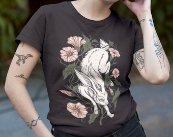 Könnte beinhalten: Ein dunkelgraues T-Shirt mit einem weißen Kaninchen, das durch rosa Blumen und grüne Blätter springt. Das Kaninchen hat einen langen Schwanz und eine lange Schnauze. Die Blumen blühen und haben ein zartes Design.