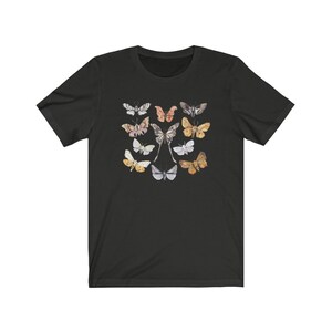 May include: Black t-shirt featuring a collection of watercolor butterflies in various colors. The butterflies are arranged in a symmetrical pattern, with a central pair and surrounding specimens in shades of pink, gold, and gray.