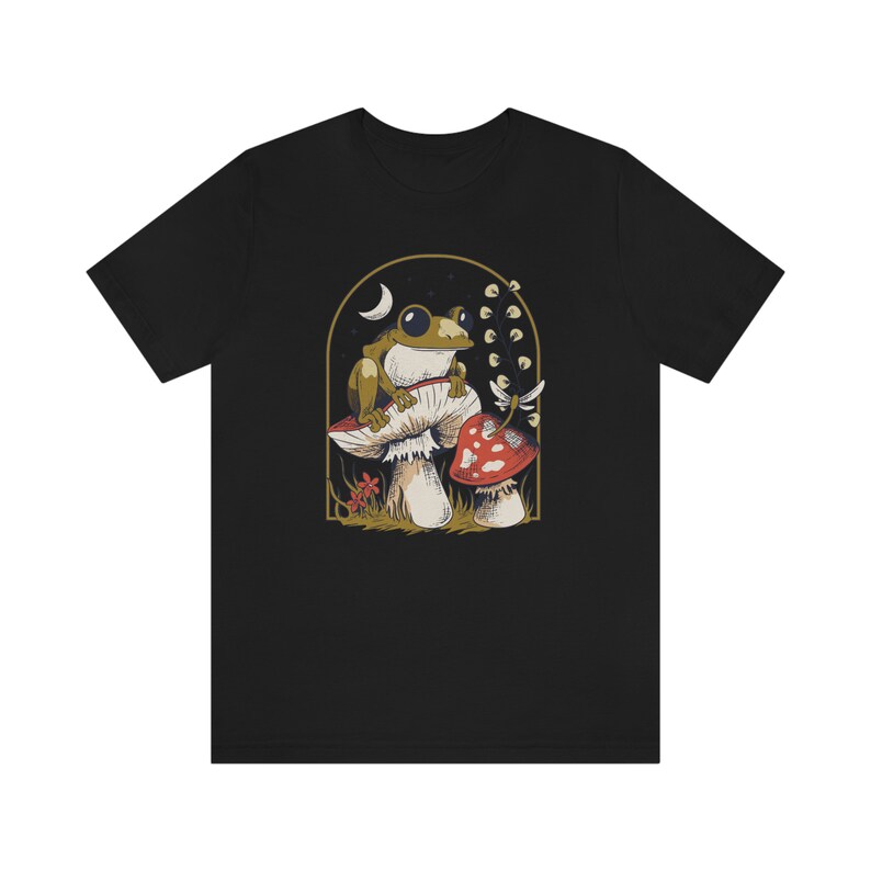 May include: Black t-shirt with a graphic of a green frog sitting on a mushroom with a red mushroom in the background.
