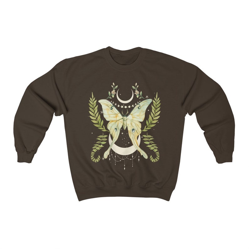 May include: A brown sweatshirt with a green and yellow butterfly design. The butterfly is centered on a crescent moon with a string of beads hanging from it. The design is surrounded by green leaves and flowers.