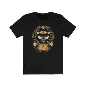 K&ouml;nnte beinhalten: Schwarzes T-Shirt mit einem floralen Kranz-Design mit einer Biene und Motten in Gelb-, Orange- und Braunt&ouml;nen.