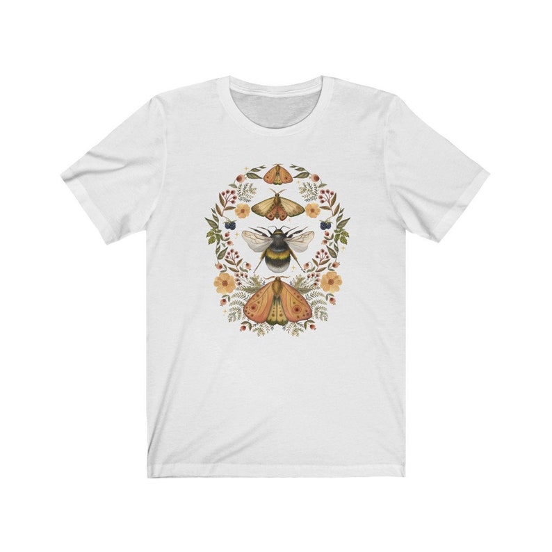 K&ouml;nnte beinhalten: Wei&szlig;es T-Shirt mit einem floralen Kranz-Design mit einer Hummel und zwei Motten. Die Motten sind orange und braun mit schwarzen Markierungen. Die Hummel ist schwarz und gelb.