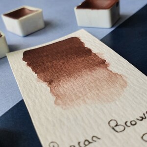 Peut inclure: Un échantillon de peinture aquarelle sur du papier blanc avec un dégradé de brun. Le texte "Pecan Brown" est écrit à l'encre noire sous l'échantillon.
