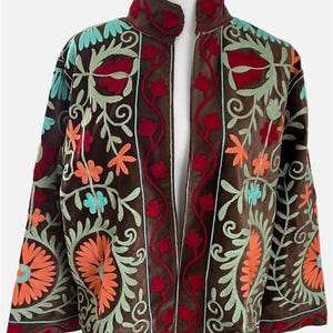 Könnte beinhalten: Eine braune Jacke mit offener Vorderseite, Stehkragen und langen Ärmeln. Das Kleidungsstück ist mit aufwendigen Blumen- und Rankenstickereien in leuchtenden Rot-, Orange-, Hellgrün- und Türkistönen über die gesamte Oberfläche verziert.