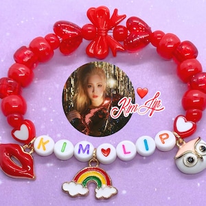 May include: Red heart bead bracelet with a rainbow charm, a red lip charm, an owl charm, and white letter beads spelling "KIM LIP". The bracelet also has a red bow and a small photo of a woman.