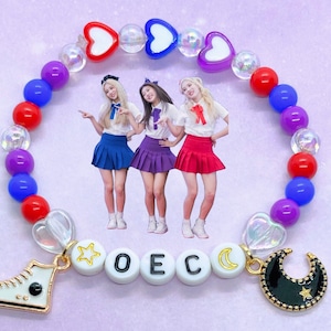 May include: A colourful beaded bracelet with red, blue and purple beads, featuring a white sneaker charm, a gold star charm, white letter beads spelling "OEC", a crescent moon charm, and a black crescent moon charm with a gold star.