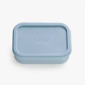 May include: A light blue rectangular silicone container with the name "Noah" embossed on the lid.