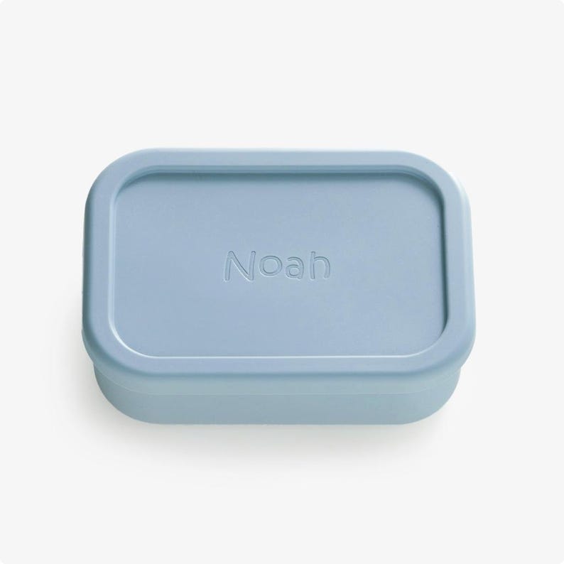 May include: A light blue rectangular silicone container with the name "Noah" embossed on the lid.