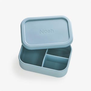 May include: A light blue silicone lunch box with a divided interior and a lid that says "Noah".