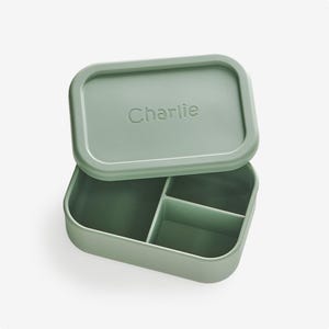 May include: A green silicone lunch box with a divided interior and a lid that says "Charlie" on it.