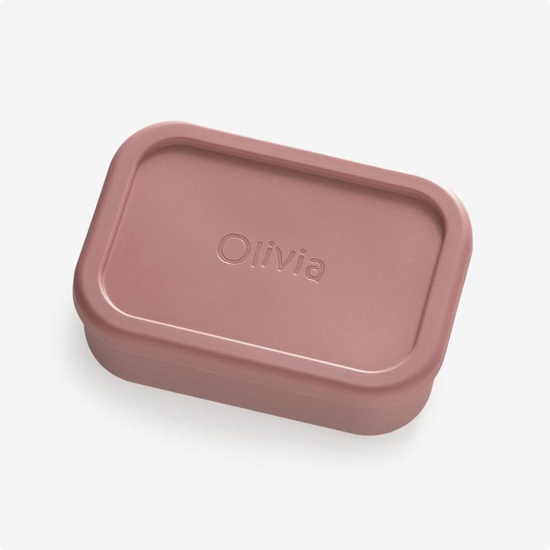 May include: A dusty rose rectangular silicone container with the name "Olivia" embossed on the lid.