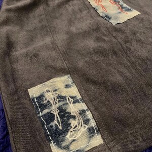May include: A dark grey skirt with two rectangular patches. Each patch features an embroidered design of koi carp. The patches are sewn onto the skirt with white thread. The skirt has a vertical seam down the centre.