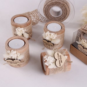 Pu&ograve; includere: Portacandele in legno decorati con juta, fiori secchi ed etichette personalizzate a forma di cuore. Le etichette riportano la scritta "Kelsey & Collin 08.16.2022".