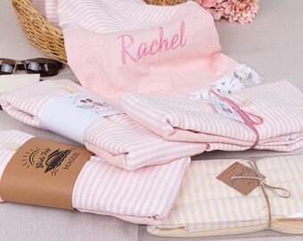 May include: Three pink and white striped towels with the names "Rachel", "Maggie", and "Girls Trip" embroidered on them. The towels are folded and tied with twine.