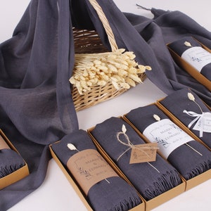 May include: Six grey scarves in brown boxes with white labels that say "Marry & Edward 2023" and a small dried flower sprig on top of each scarf.