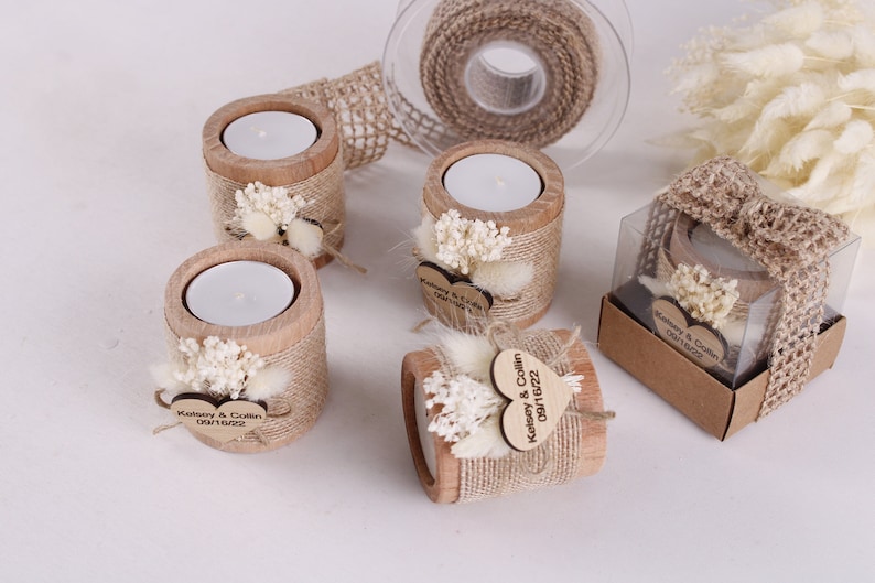 Pu&ograve; includere: Portacandele in legno decorati con juta, fiori secchi ed etichette personalizzate a forma di cuore. Le etichette riportano la scritta "Kelsey & Collin 08.16.2022".