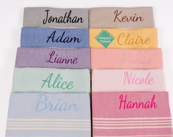 May include: A stack of ten personalized towels with different names embroidered on each towel. The towels are in various colors, including gray, blue, purple, green, pink, and yellow. The towels have a striped pattern and are made of a soft, absorbent material.