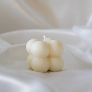 May include: A white, round, bubble-shaped candle with a single wick.