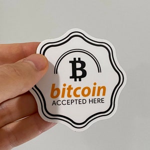 May include: White sticker with a black border and a stylized black Bitcoin symbol with a yellow "B". The text "bitcoin ACCEPTED HERE" is in black and yellow.