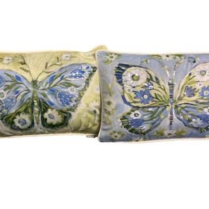 May include: Two rectangular decorative pillows with butterfly designs. One pillow has a light green background with a blue butterfly. The other pillow has a light blue background with a butterfly design and sequins.