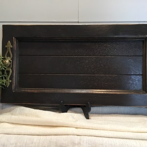May include: A black wooden serving tray with two ornate brass handles. The tray is distressed and has a rustic look.