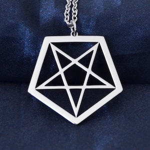 Può includere: Collana con pendente argentato con un design geometrico a pentagono e una stella a cinque punte all'interno. Il pendente è appeso a una delicata catena su uno sfondo blu scuro, creando un contrasto sorprendente. Un gioiello.