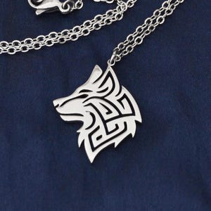 May include: A silver-toned metal necklace featuring a pendant shaped like a stylised wolf head with intricate geometric cut-out patterns. The pendant is attached to a delicate silver-toned chain with a lobster claw clasp closure mechanism.