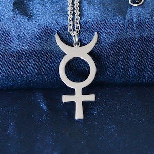 Può includere: Una collana in metallo color argento con un ciondolo a forma di simbolo astrologico di Mercurio, composto da un cerchio con una croce alla base e una mezzaluna sulla parte superiore, sospeso a una catena a maglie abbinata.