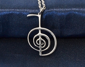 May include: A silver necklace with a pendant in the shape of a stylized symbol. The symbol is a circle with a spiral inside, and a vertical line extending from the top of the circle.
