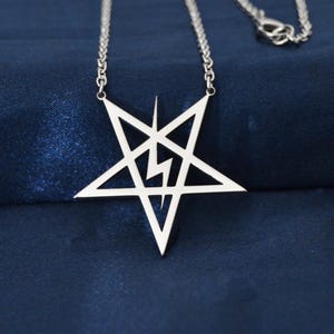 Peut inclure: Un collier argenté avec un pendentif en forme de pentagramme et un éclair. Le pendentif est suspendu à une chaîne délicate sur un fond bleu foncé. Un bijou.