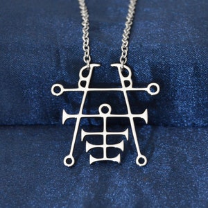 May include: A silver pendant necklace with a geometric design. The pendant is shaped like a cross with a circle in the center and four arms extending out from the circle. The arms are decorated with small circles and triangles.