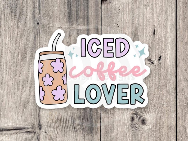 Puede incluir: Una pegatina con las palabras "ICED coffee LOVER" en colores pastel. El dise&ntilde;o incluye un caf&eacute; helado de dibujos animados con detalles florales. El fondo es una superficie de madera.