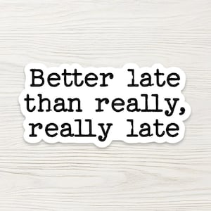 May include: A white sticker with black text that reads "Better late than really, really late." The sticker has a rounded rectangular shape and is set against a light wood grain background.